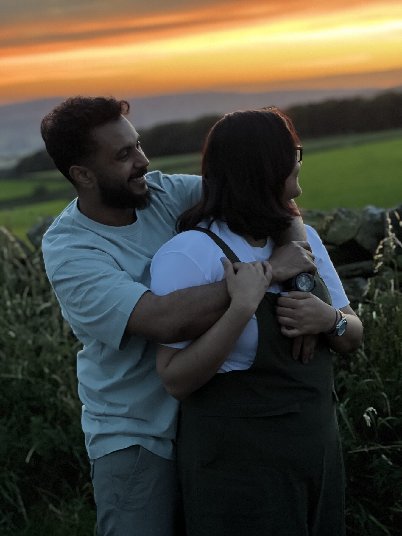 Aswin and Hridhya holding each other in the countryside at golden hour